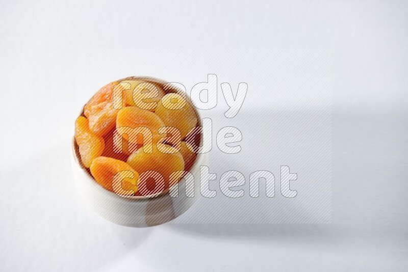 A beige ceramic bowl full of dried apricots on a white background in different angles