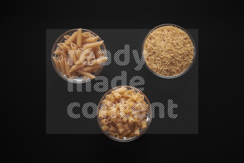 Different pasta types in glass bowls on black background