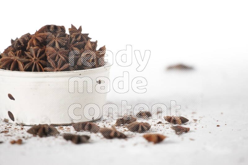 Star Anise in a white bowl and more of it sprinkled on white background