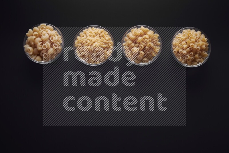 Different pasta types in glass bowls on black background