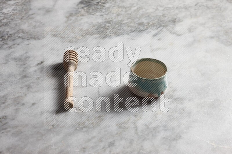 Multicolored pottery bowl with wooden honey dipper on the side on grey marble background