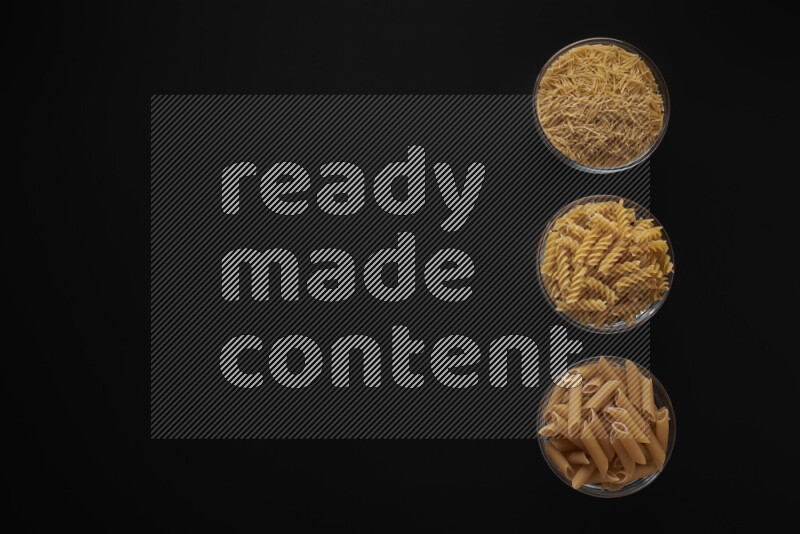 Different pasta types in 3 glass bowls on black background