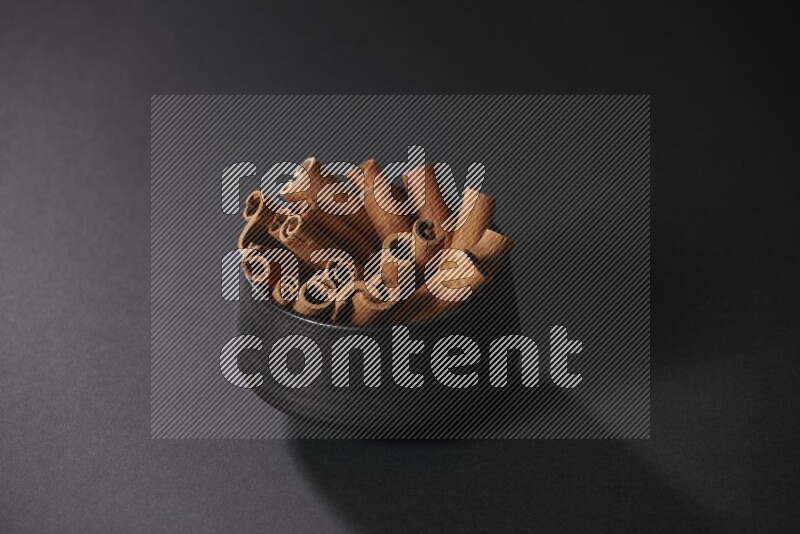 Cinnamon sticks in a black bowl on a black background in different angles