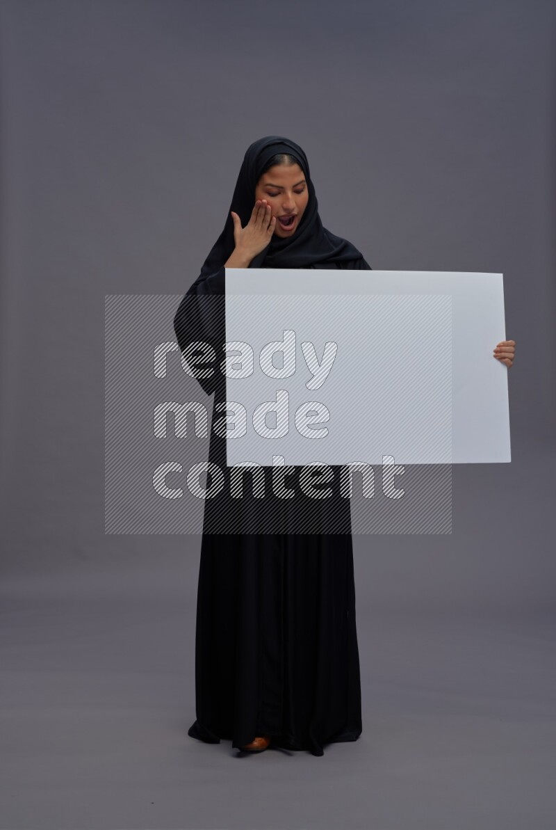Saudi woman wearing Abaya standing holding white board on gray background