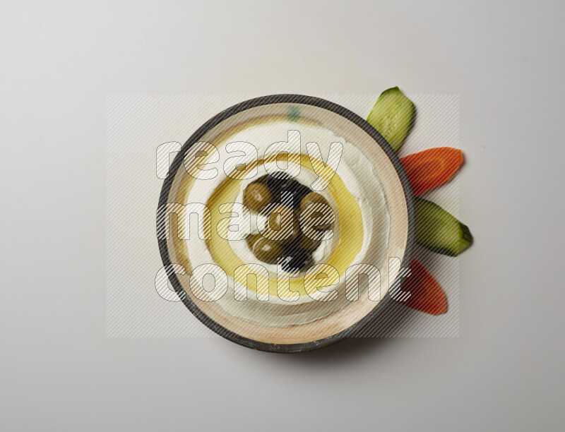 Lebnah garnished with whole black olives in a pottery plate on a white background