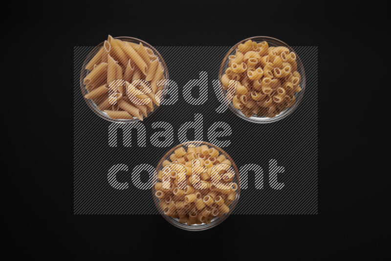 Different pasta types in glass bowls on black background