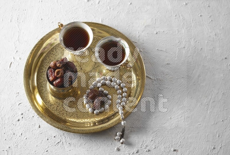 Dates in a metal bowl with tea and prayer beads on a tray in a light setup