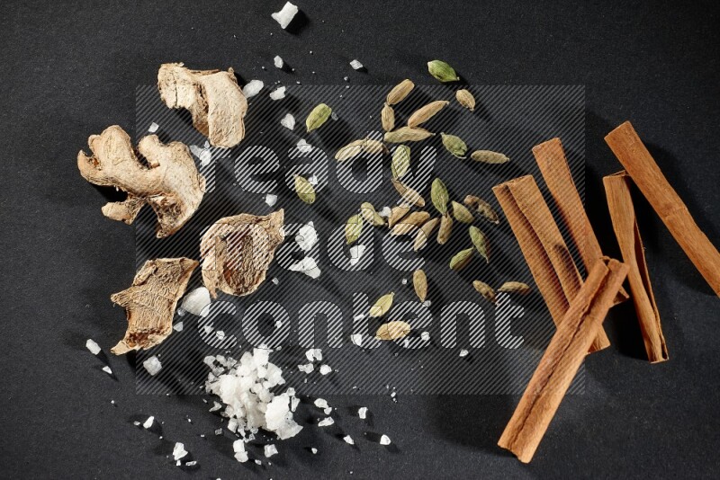 Ginger, salt, cardamom and cinnamon sticks on black flooring