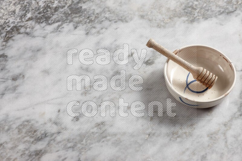 Multicolored pottery bowl with wooden honey dipper in it on grey marble background