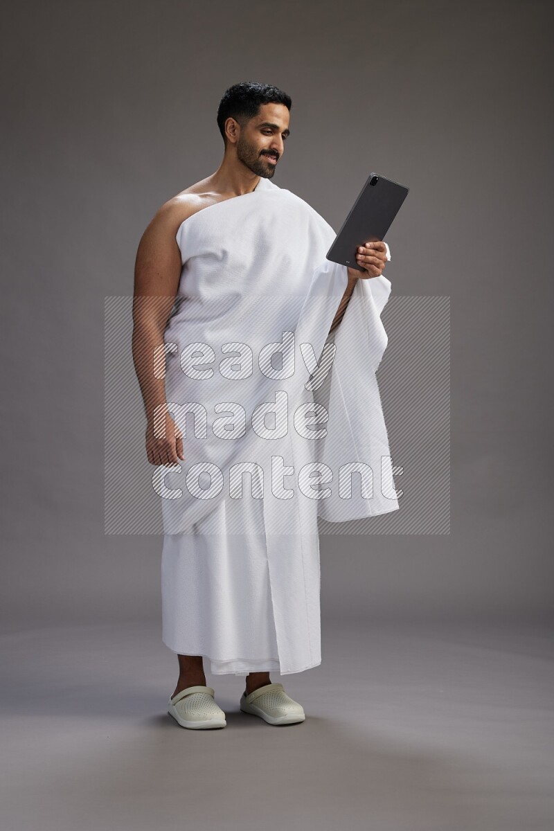A man wearing Ehram and holding a tablet on gray background