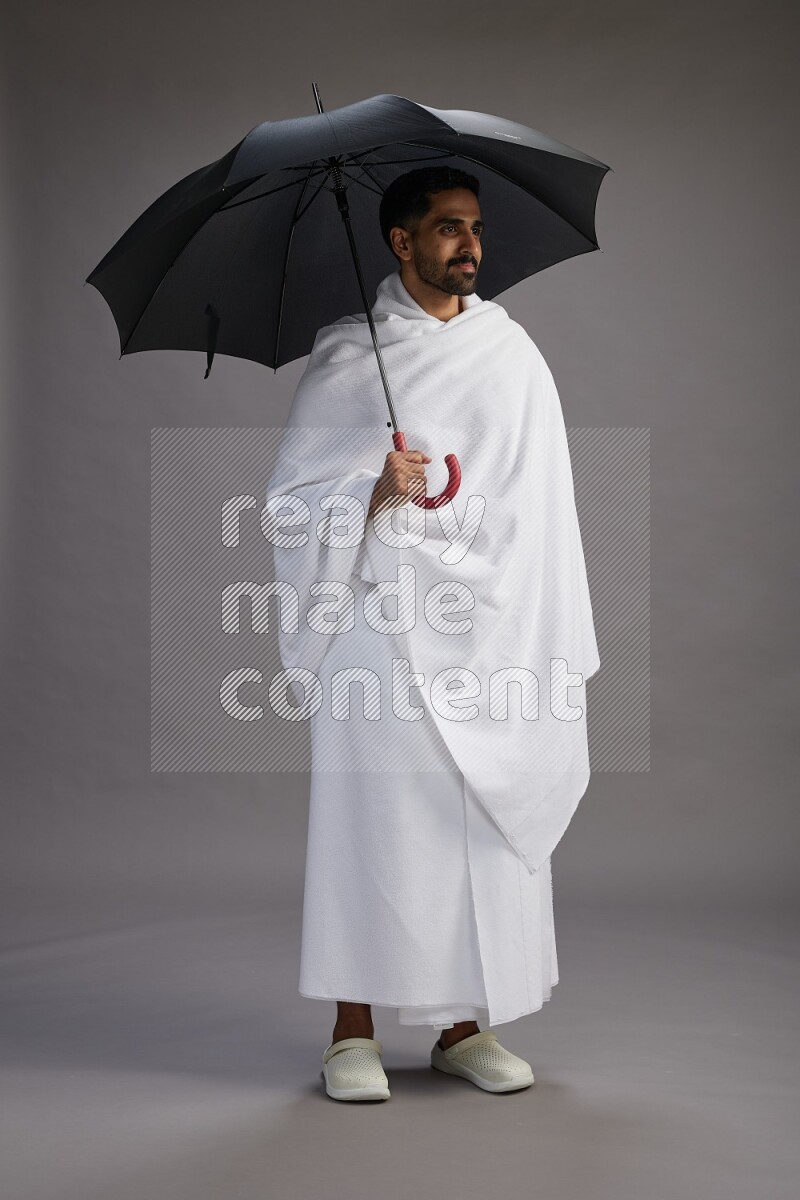 A man wearing Ehram Standing holding umbrella on gray background