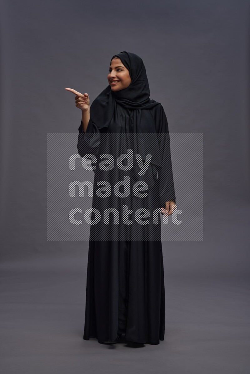 Saudi woman wearing Abaya standing interacting with the camera on gray background