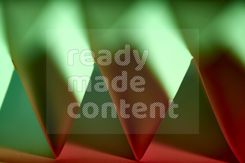 A close-up abstract image showing sharp geometric paper folds in green and red gradients
