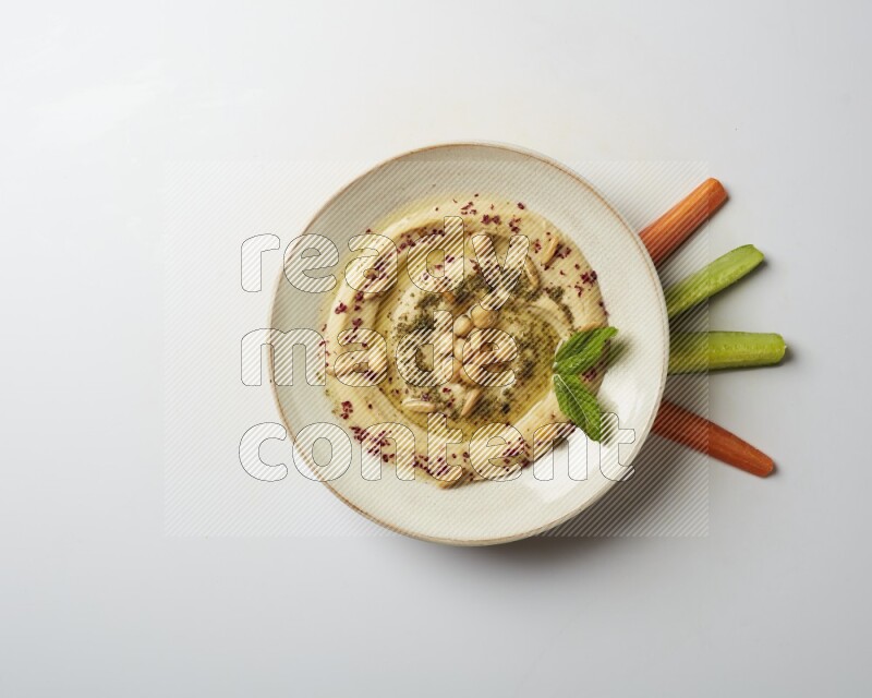 Hummus in a pottry plate garnished with zaatr & sumak on a white background