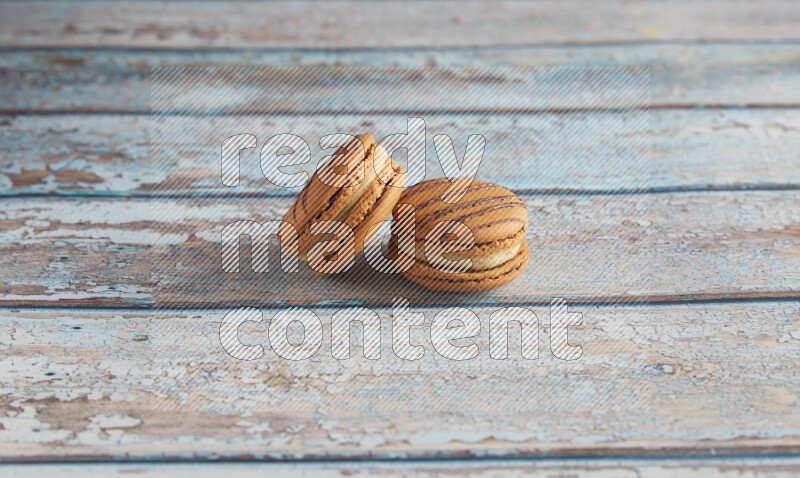 45º Shot of two light brown Almond Cream macarons on light blue wooden background