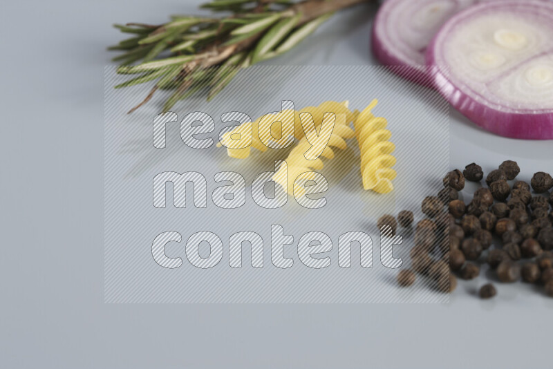 Raw pasta with different ingredients such as cherry tomatoes, garlic, onions, red chilis, black pepper, white pepper, bay laurel leaves, rosemary, cardamom and mushrooms on light blue background