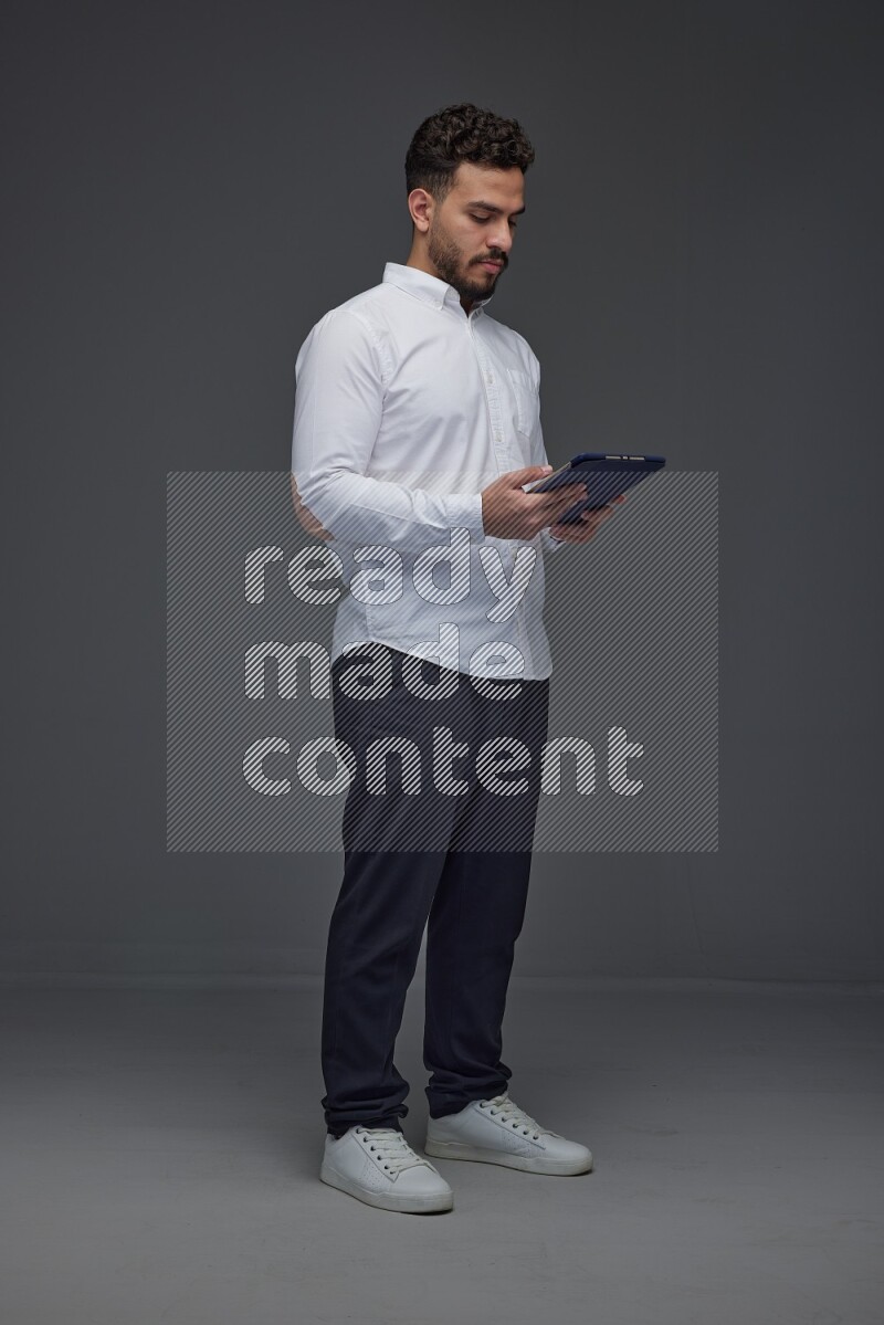 A man wearing smart casual standing and using his tablet eye level on a gray background