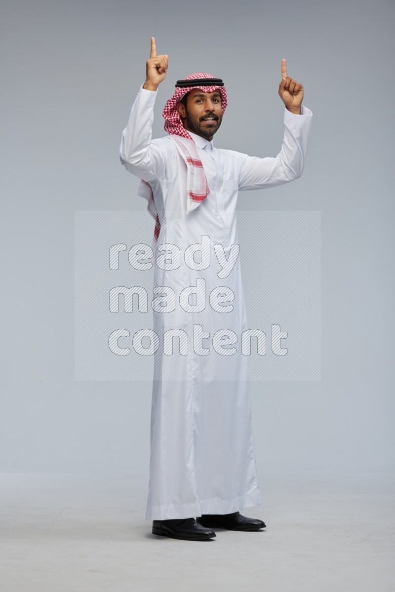Saudi man Wearing Thob and shomag standing interacting with the camera on Gray background