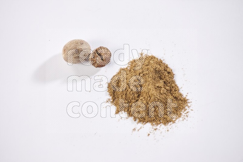 Nutmeg whole seeds with nutmeg powder beside it on a white flooring