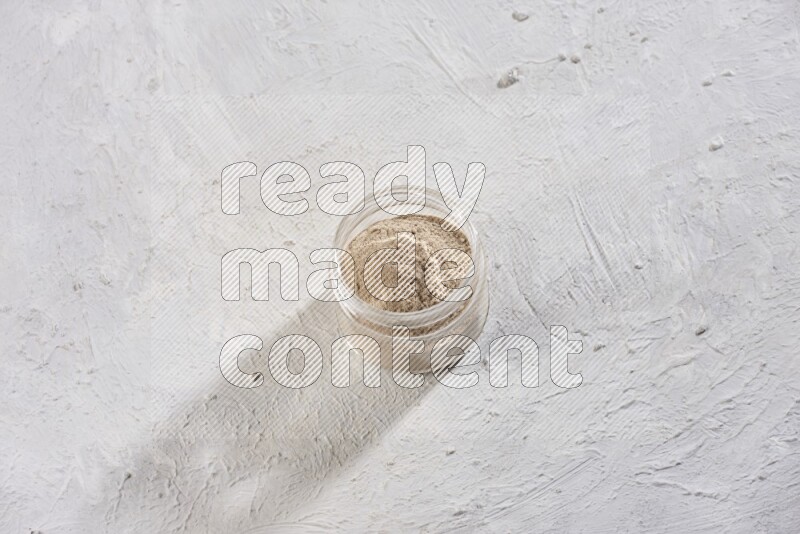 A glass jar full of garlic powder on a textured white flooring