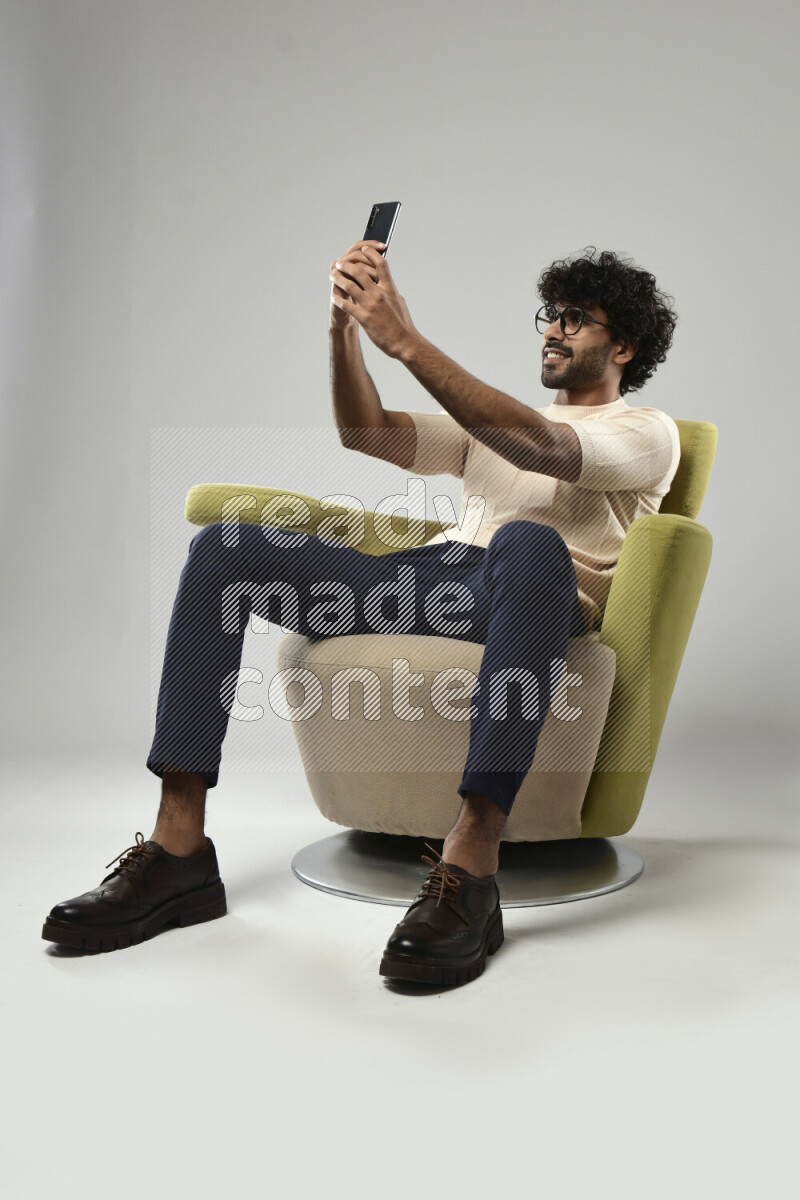 A man wearing casual sitting on a chair taking a selfie on white background