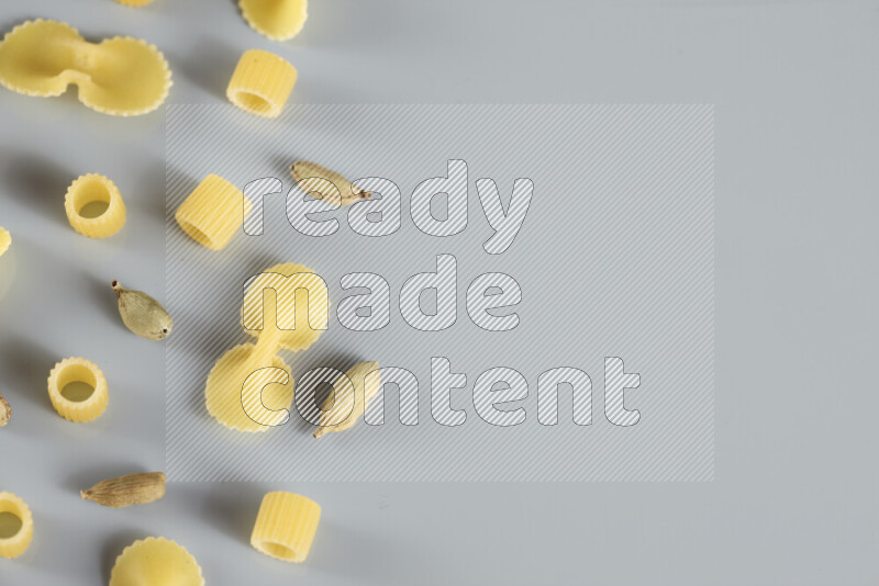 Raw pasta with different ingredients such as cherry tomatoes, garlic, onions, red chilis, black pepper, white pepper, bay laurel leaves, rosemary, cardamom and mushrooms on light blue background