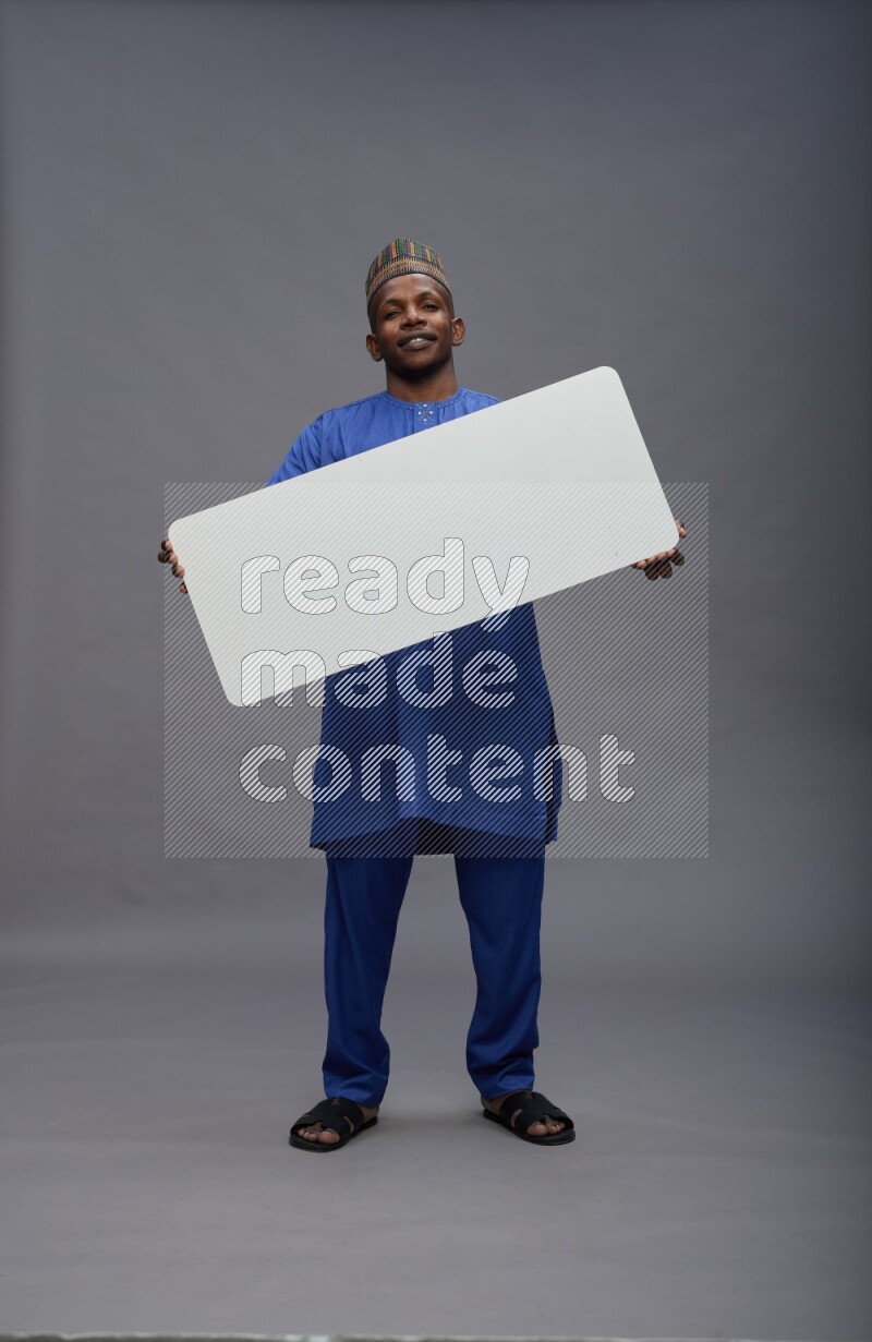 Man wearing Nigerian outfit standing holding board on gray background