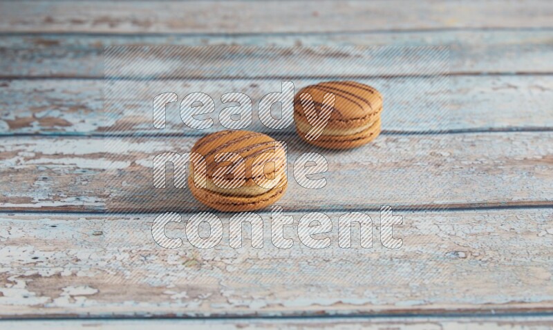 45º Shot of two light brown Almond Cream macarons on light blue wooden background