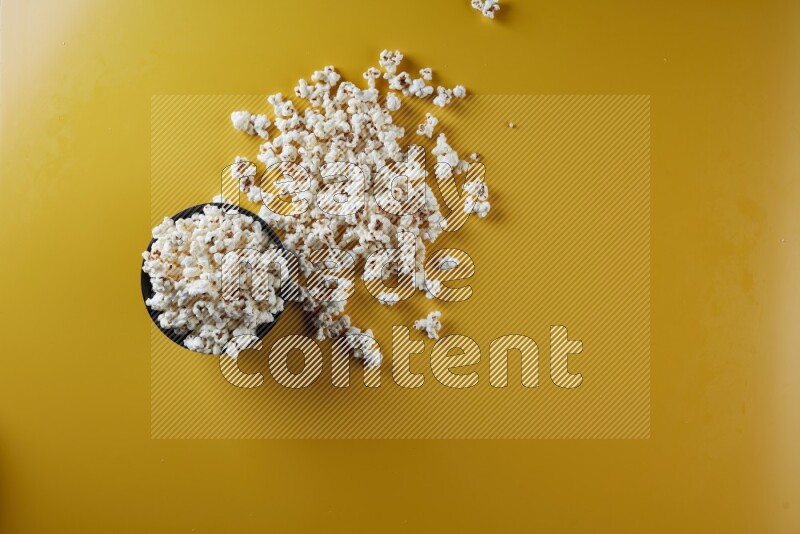 A black ceramic bowl full of popcorn with popcorn beside it on a yellow background in different angles