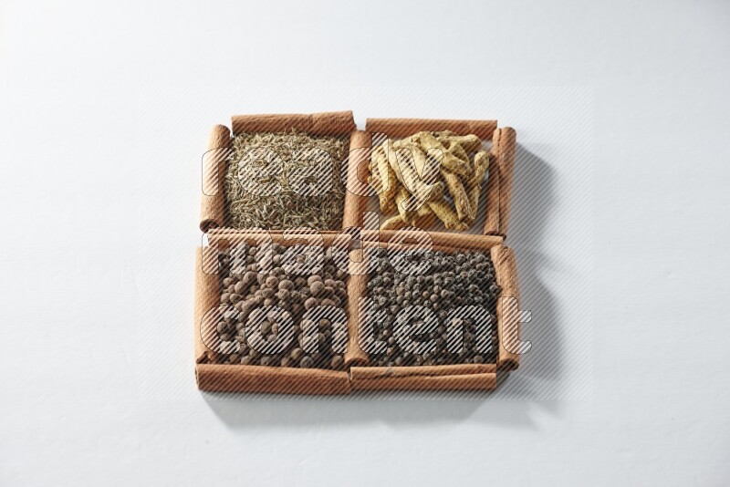 4 مربعات من أعواد القرفة ممتلئة بالكمون وأصابع الكركم وبهار الفلفل الحلو وحبوب الفلفل الأسود على أرضية بيضاء