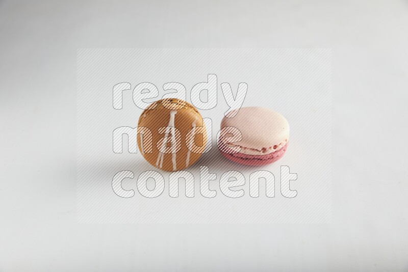 45º Shot of of two assorted Brown Irish Cream, and Pink Litchi Raspberry macarons on white background
