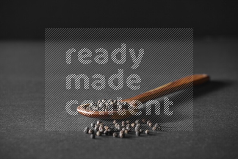 حبوب الفلفل الأسود في مغرفة خشبية علي خلفية سوداء