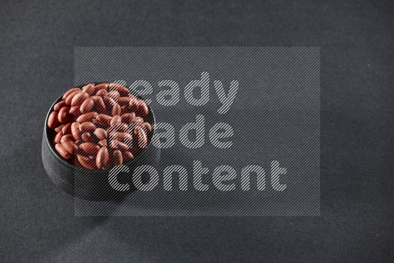 A black pottery bowl full of red skin peanuts on a black background in different angles