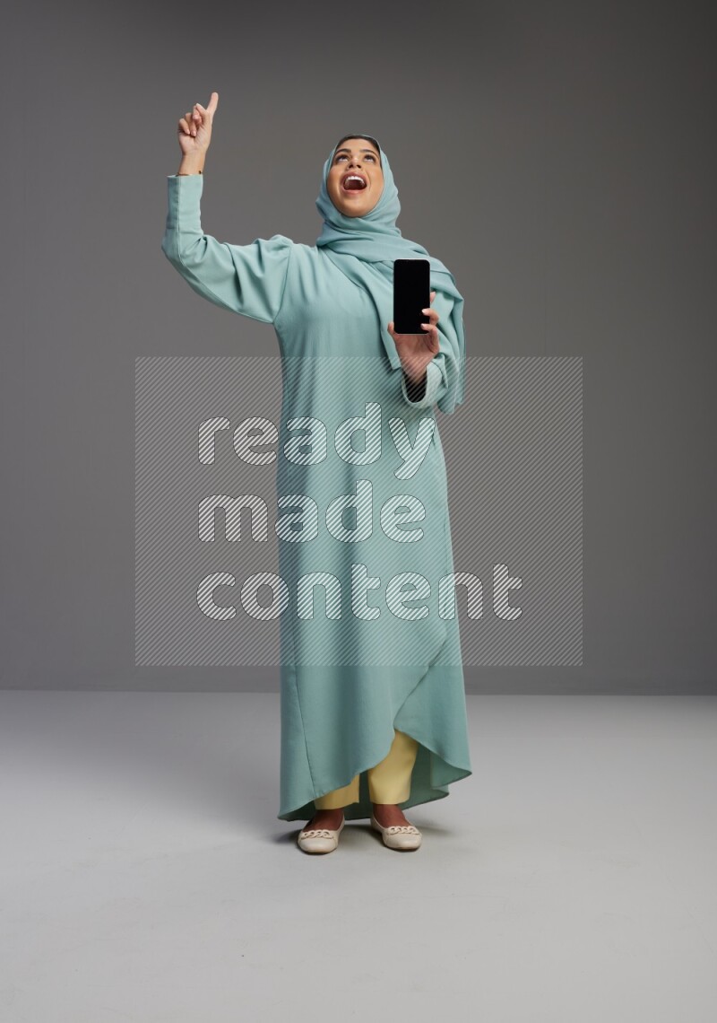 Saudi Woman wearing Abaya standing showing phone to camera on Gray background