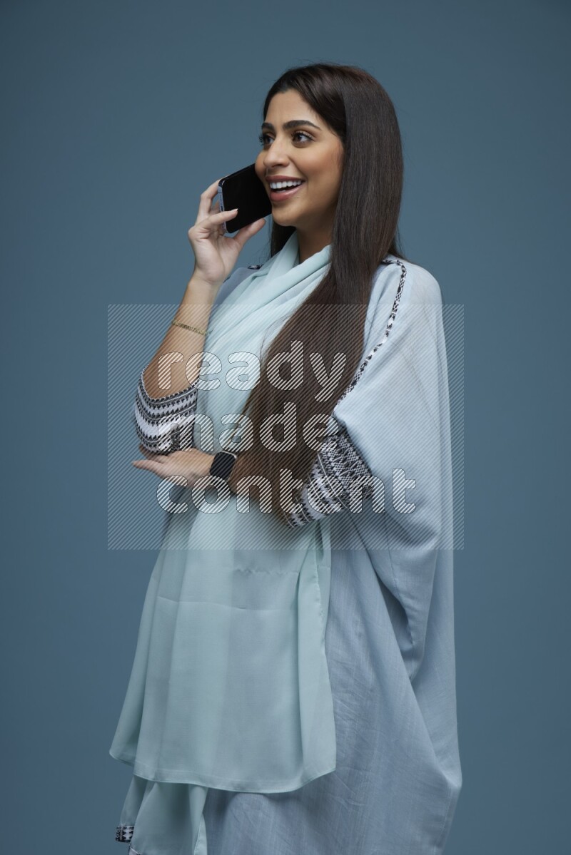 A Saudi woman having a Call in a blue background wearing a blue Abaya with no hijab