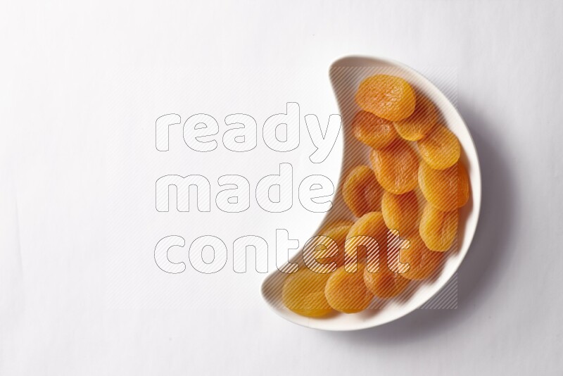 Dried apricots in a crescent pottery plate on white background