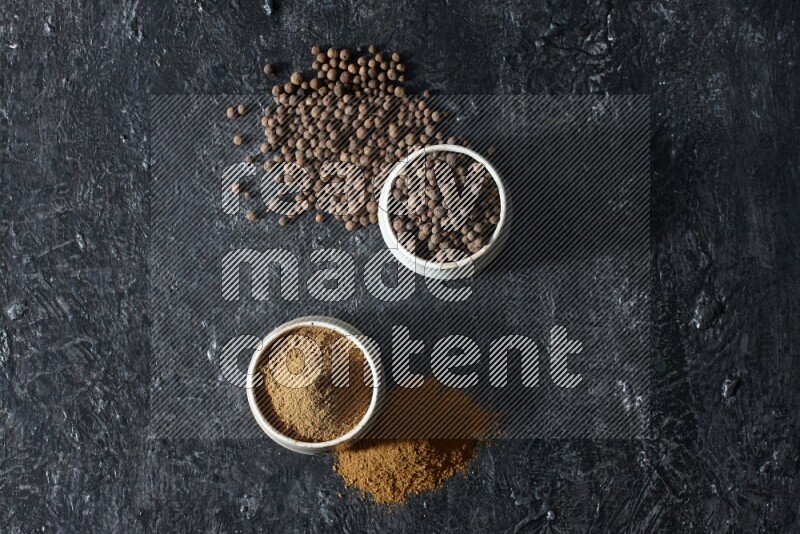 2 beige bowls, one full of allspice powder and the other full of whole balls and both spread on a textured black flooring