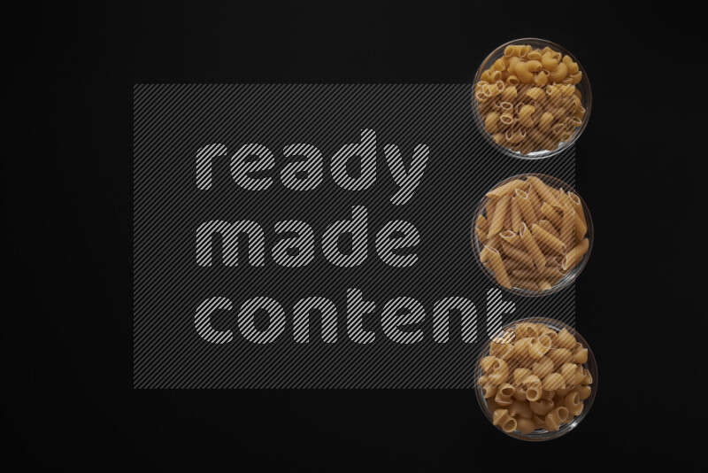 Different pasta types in 3 glass bowls on black background