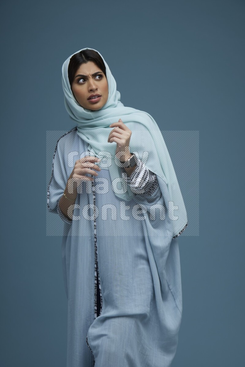 A woman posing in a blue background wearing a blue Abaya with hijab