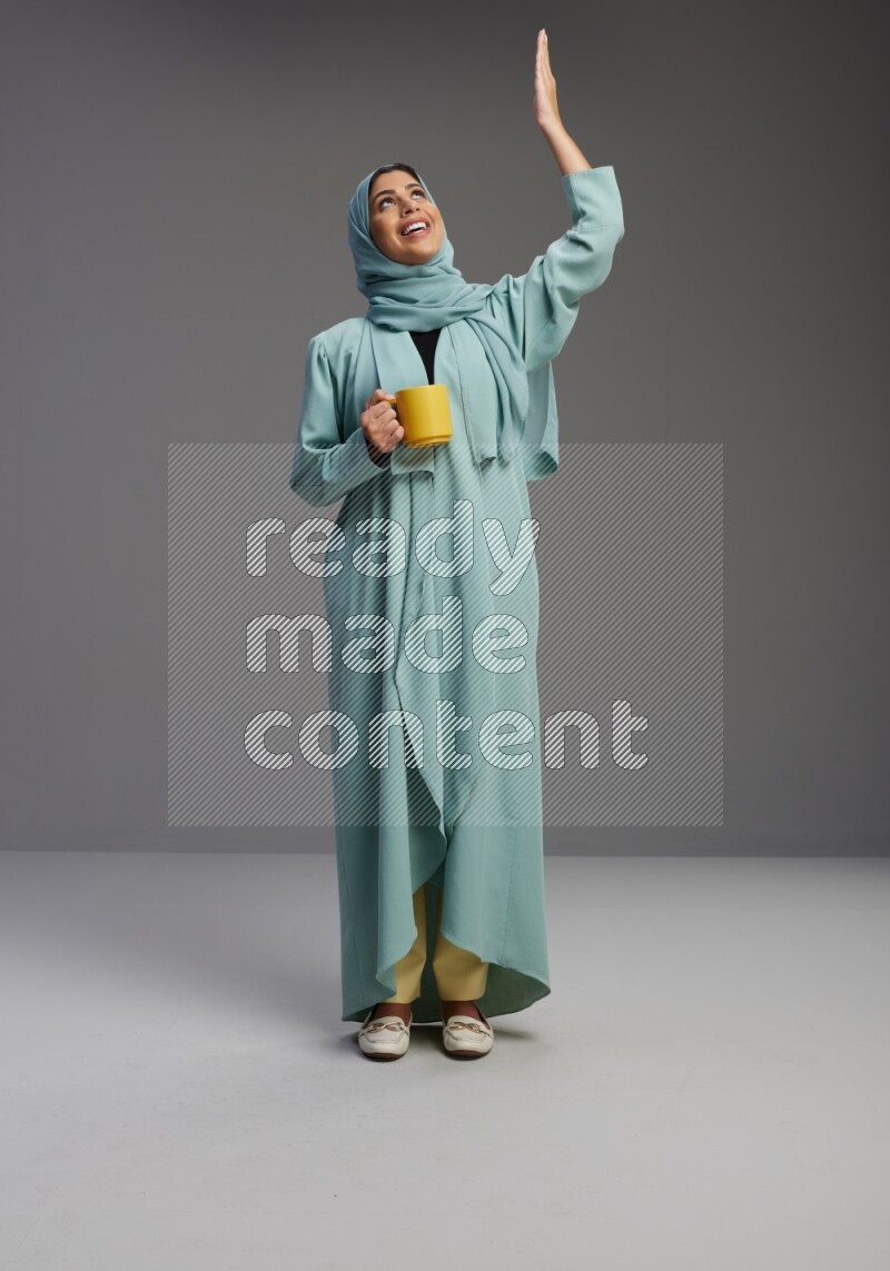 Saudi Woman wearing Abaya standing  holding a mug on Gray background