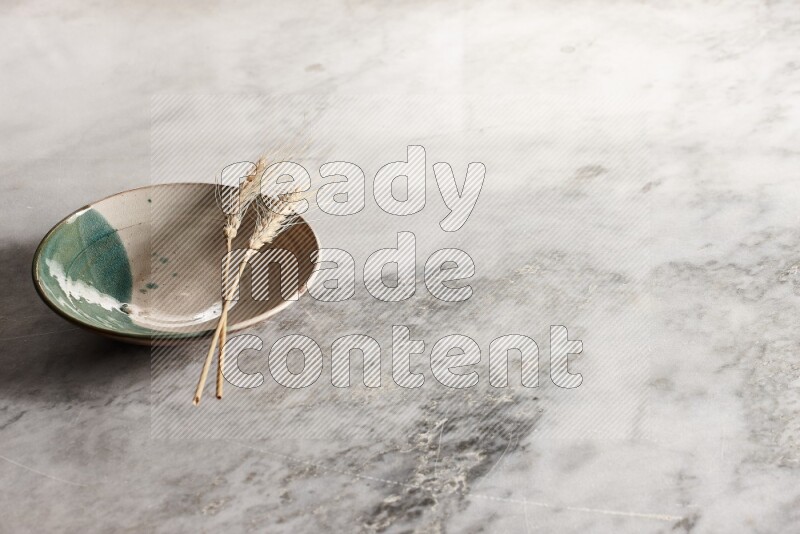 Wheat stalks on multicolored pottery plate on grey marble background
