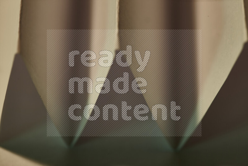A close-up abstract image showing sharp geometric paper folds in green gradients and warm tones