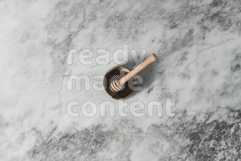 Brown pottery bowl with wooden honey dipper in it on grey marble background