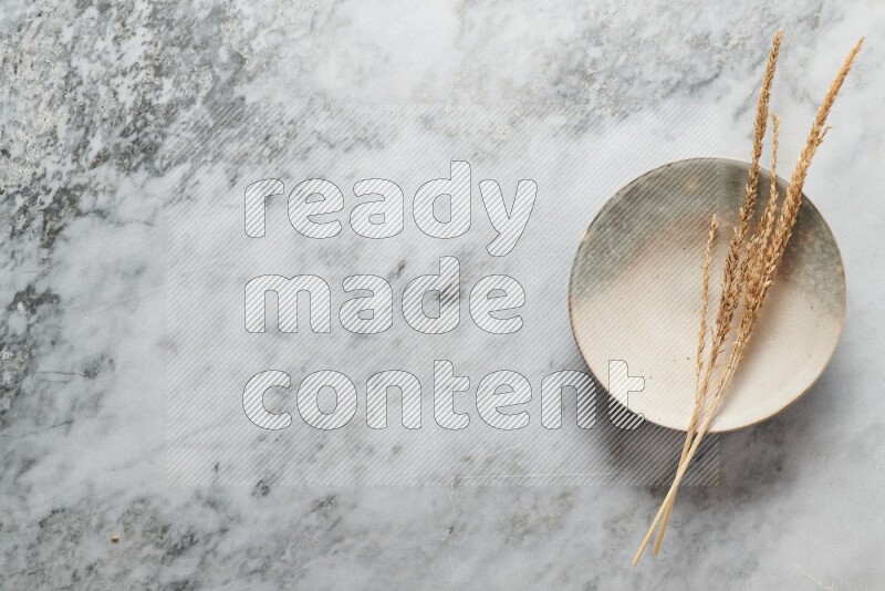 Wheat stalks on multicolored pottery plate on grey marble background