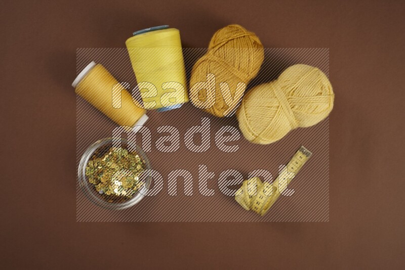 A yellow collection of sewing and tailoring tools arranged on a brown background
