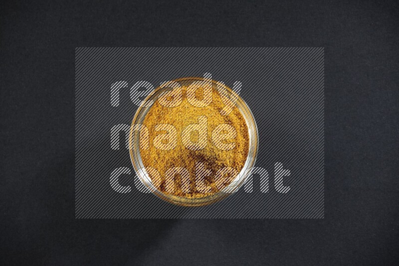 A glass bowl full of turmeric powder on black flooring