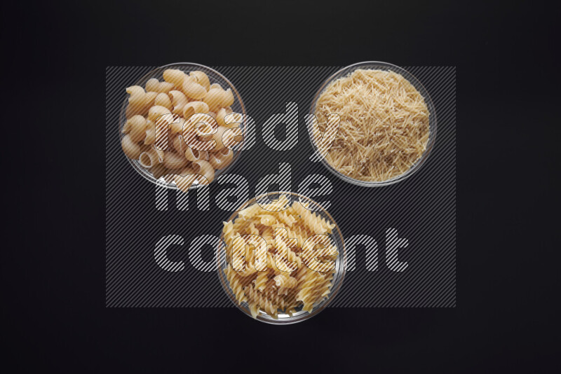 Different pasta types in glass bowls on black background