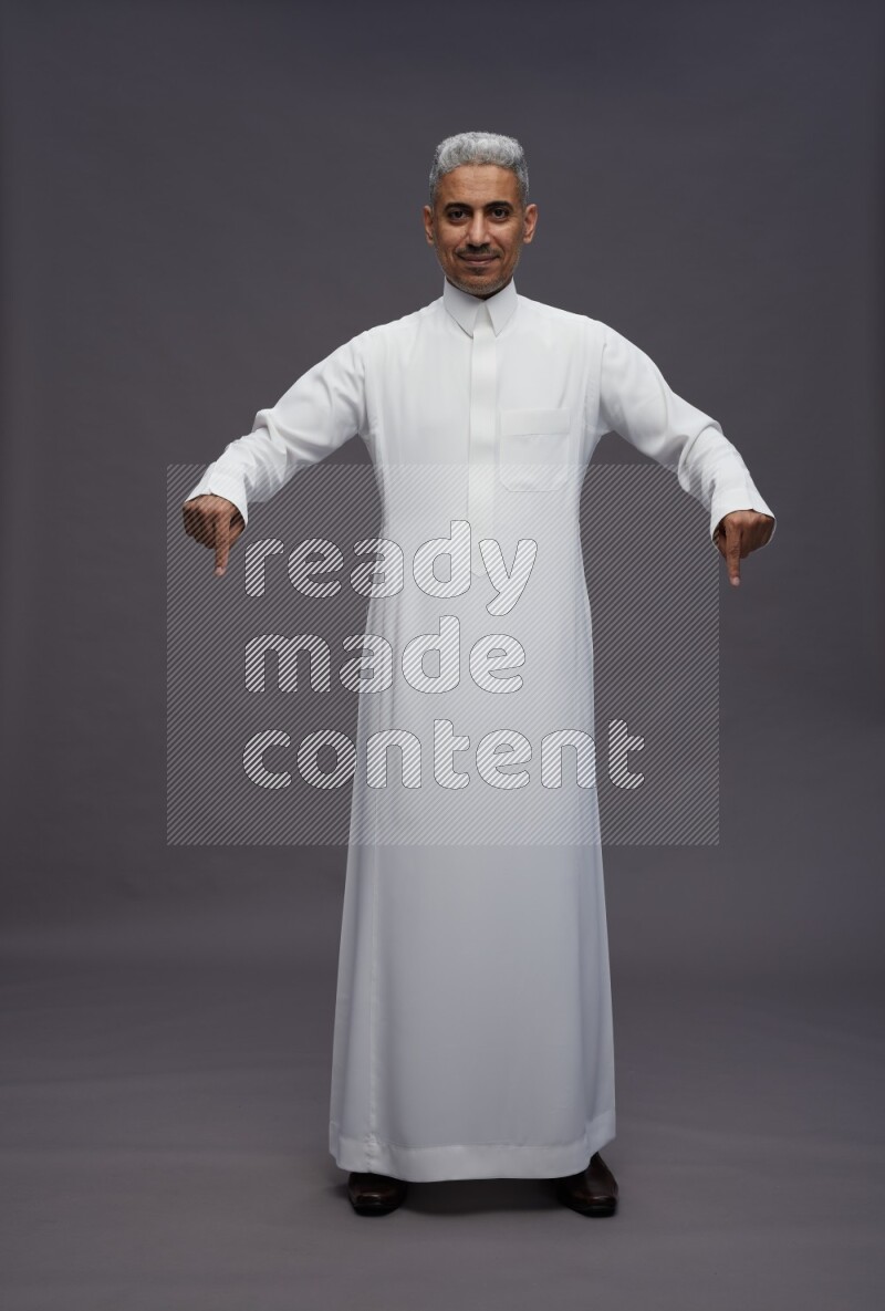 Saudi man wearing thob standing interacting with the camera on gray background