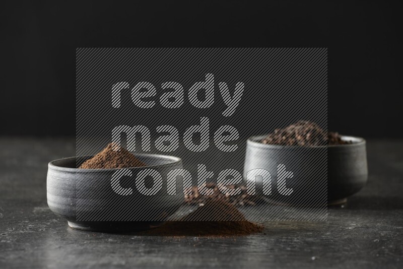 وعاءين من الفخار الأسود أحدهما ممتلئي بحبوب القرنفل والآخر ممتلئ ببودرة القرنفل على خلفية سوداء