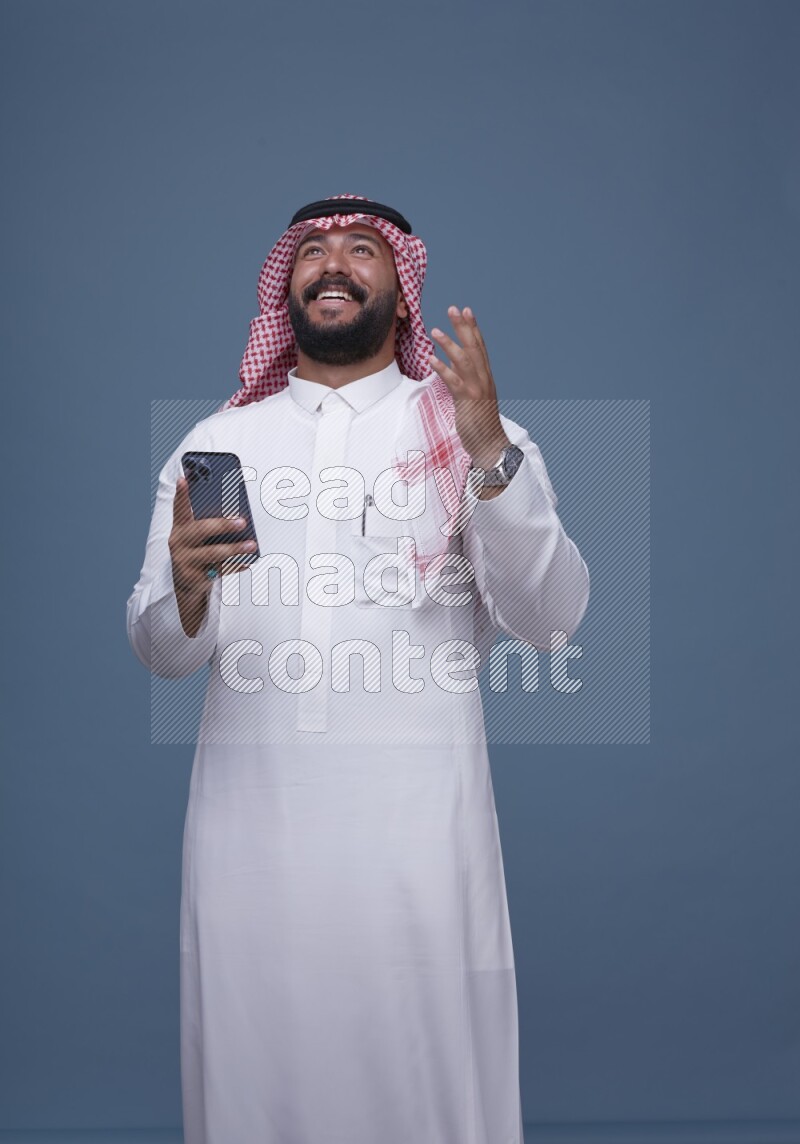 A man Texting on Blue Background wearing Saudi Thob and Shomag